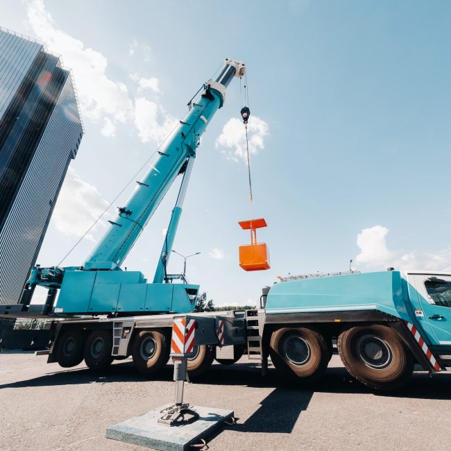 A large blue truck crane stands ready for operation on a site near a large modern building. The